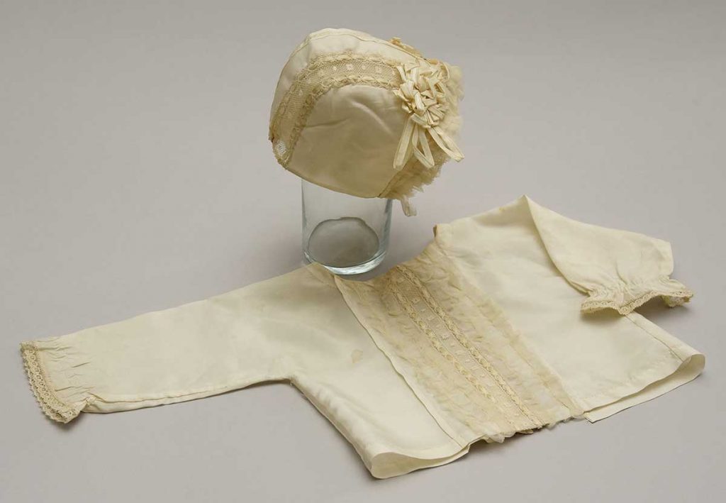 Hedvábná křticí souprava ozdobená krajkou; souprava byla zhotovena slečnami Plachetkovými pro neteř - dceru sládka Antonína Plachetky z pivovaru v Rychnově  nad Kněžnou, 1911