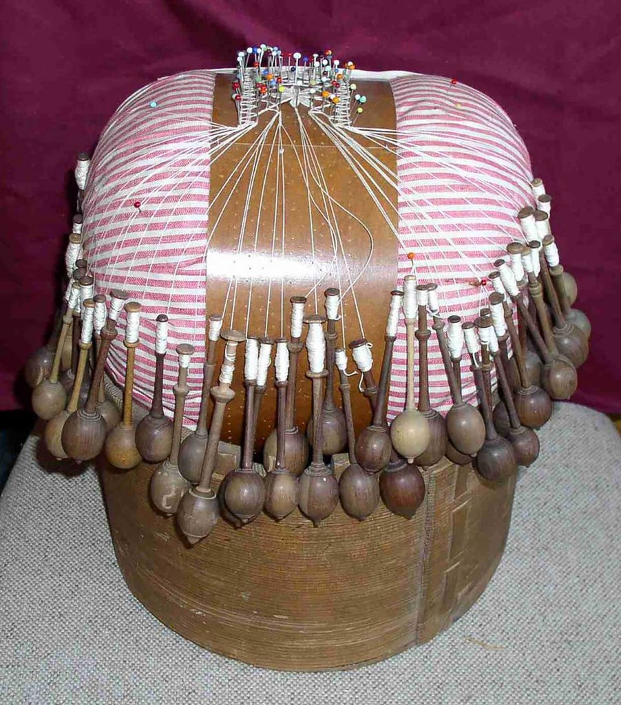 Poduška „herdule“ s podvinkem a rozpracovanou paličkovanou krajkou v dřevěném škopíčku; krajku paličkovala Antonie Hynková z Přímu, 60.léta 20. století. Poduška byla vytvořená kolem roku 1900.