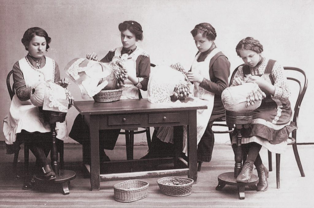 Historická fotografie 4 krajkářek v krojích s herdulemi a rozpracovanými díly